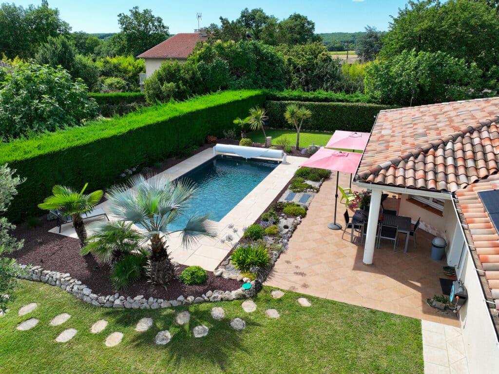 Jardin luxuriant avec piscine, palmiers et terrasse ombragée Vue aérienne d'un jardin luxuriant avec piscine bleue, palmiers, terrasse ombragée et pelouse verte avec pas japonais.