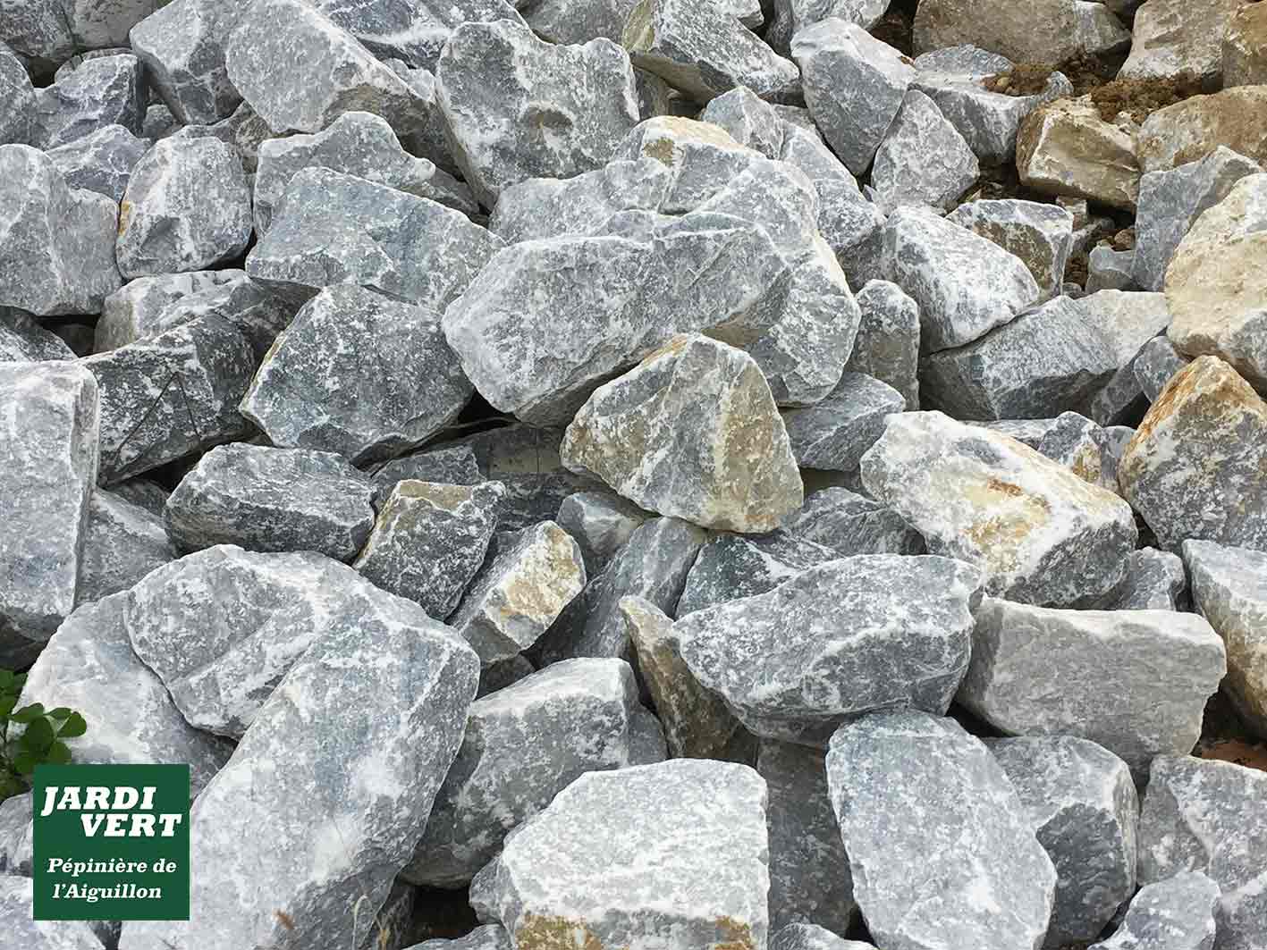 Gros plan sur un tas de roches naturelles grises et beiges, idéales pour l'aménagement paysager. Logo JARDI VERT, Pépinière de l'Aiguillon.